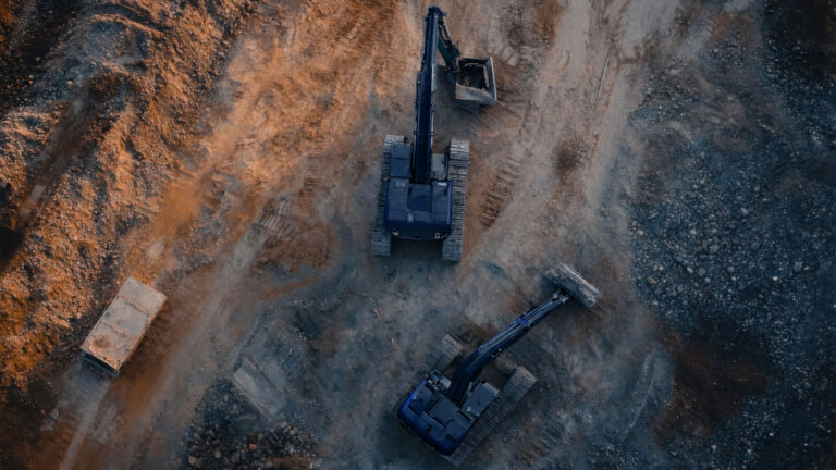 Luftaufnahme von zwei Baggern auf unebenem, erdigem Gelände mit einem Container