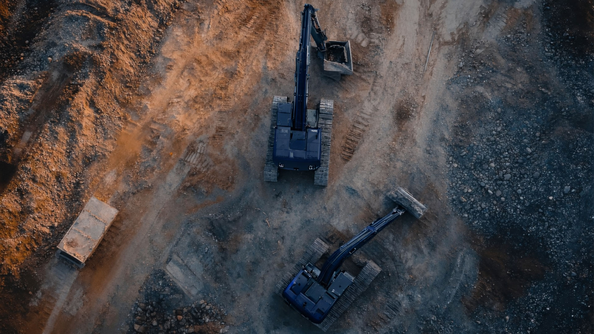 Luftaufnahme von zwei Baggern auf unebenem, erdigem Gelände mit einem Container